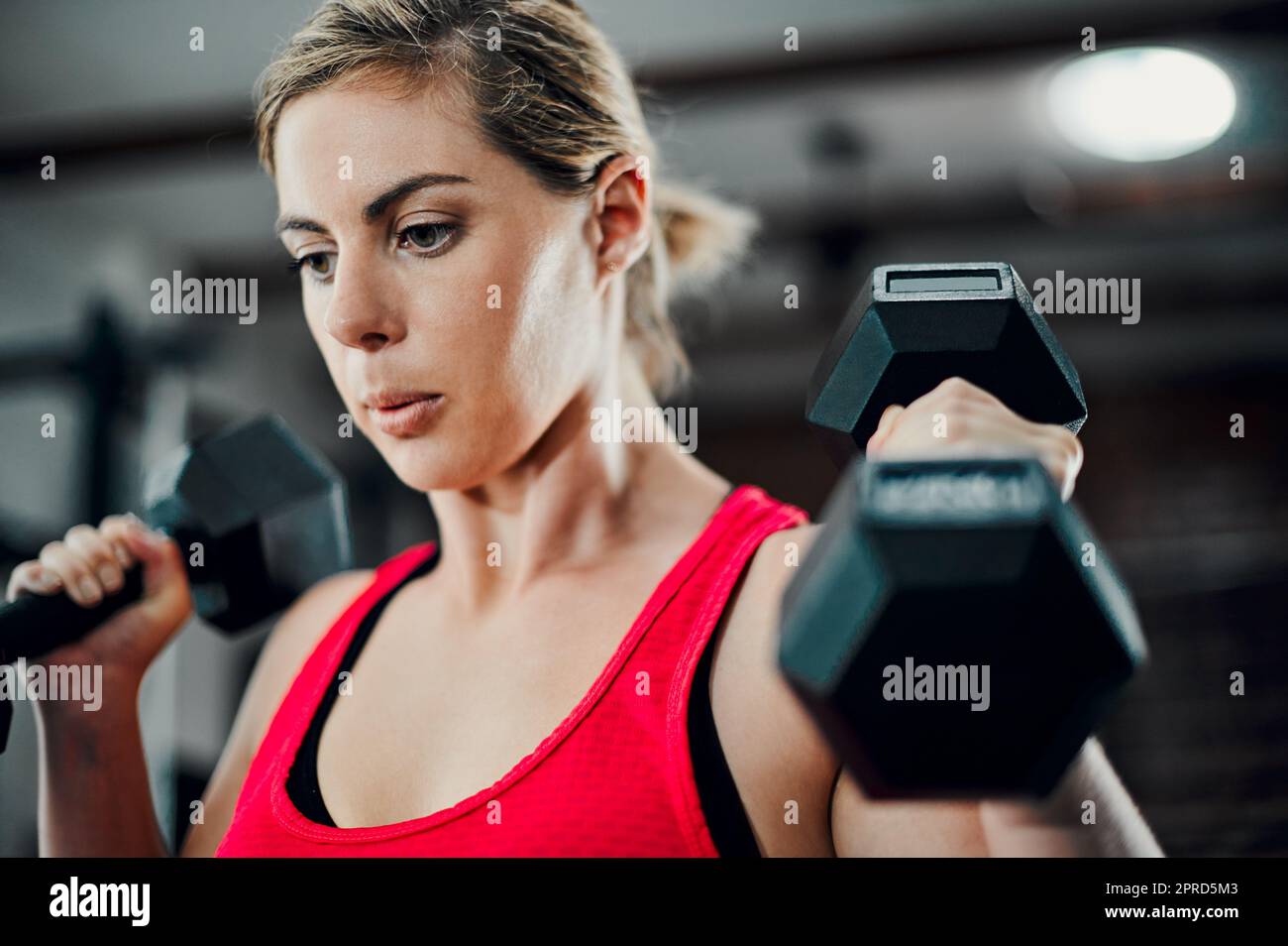 Fortalecimiento de los brazos. Una atractiva atleta joven haciendo ejercicio con pesas en el gimnasio. Foto de stock