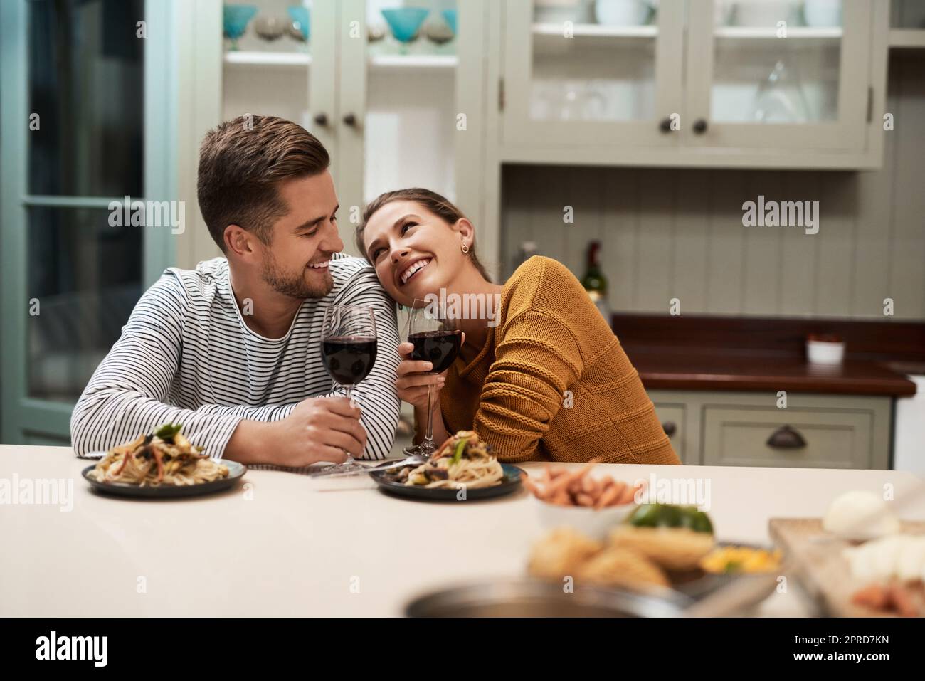 Aún así es el mejor aperitivo. Una pareja joven y cariñosa sonriendo mientras disfruta de la cena en su cocina en casa. Foto de stock