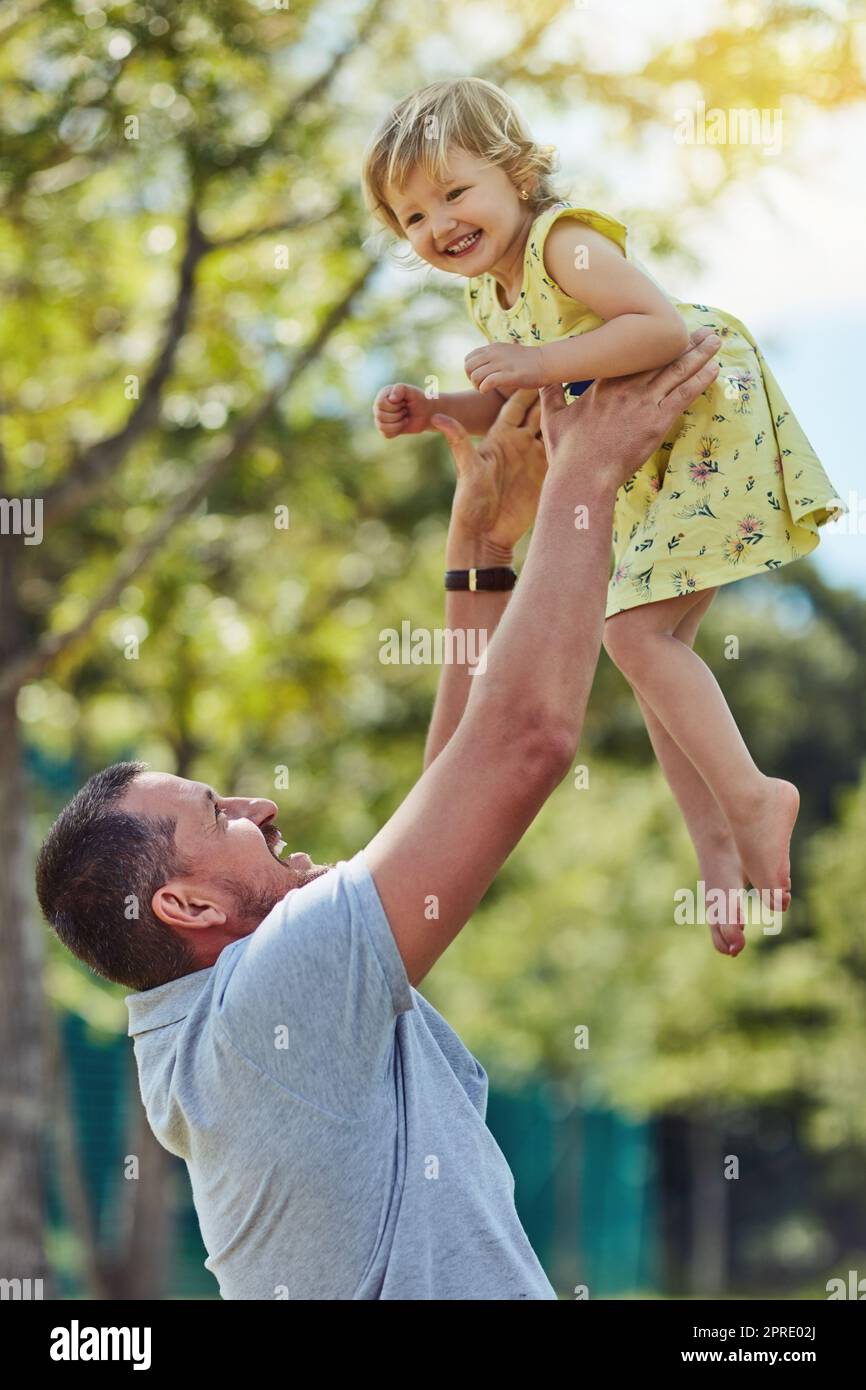Déles alas y déjelas volar. Un padre que se une con su hija pequeña al aire libre. Foto de stock