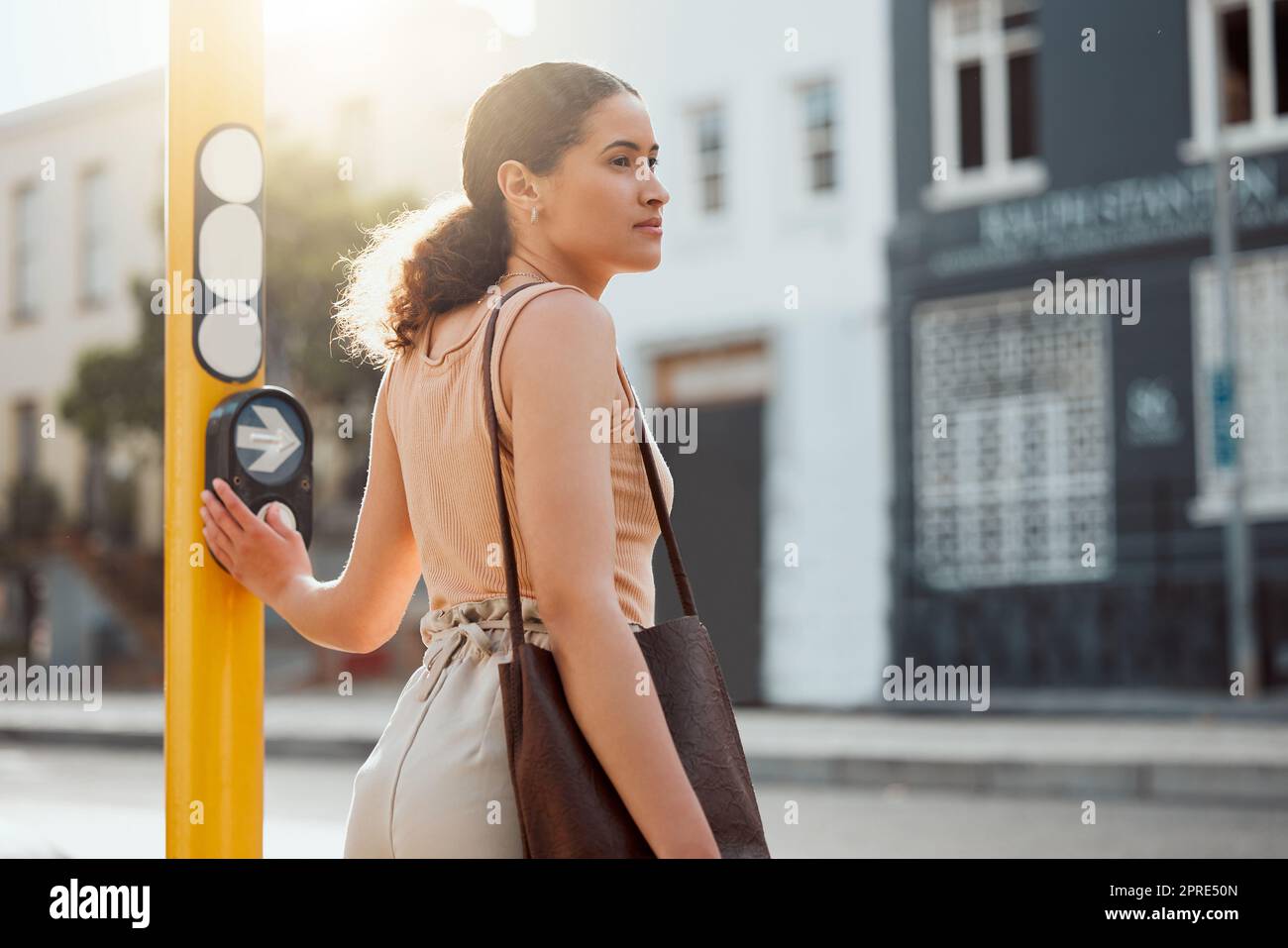 Peatón femenino atractivo listo para cruzar la calle, esperando la luz verde y presionando el botón en un cruce Mujer joven de la ciudad en un paseo de la mañana para trabajar, de pie y mirando hacia fuera para el tráfico. Foto de stock