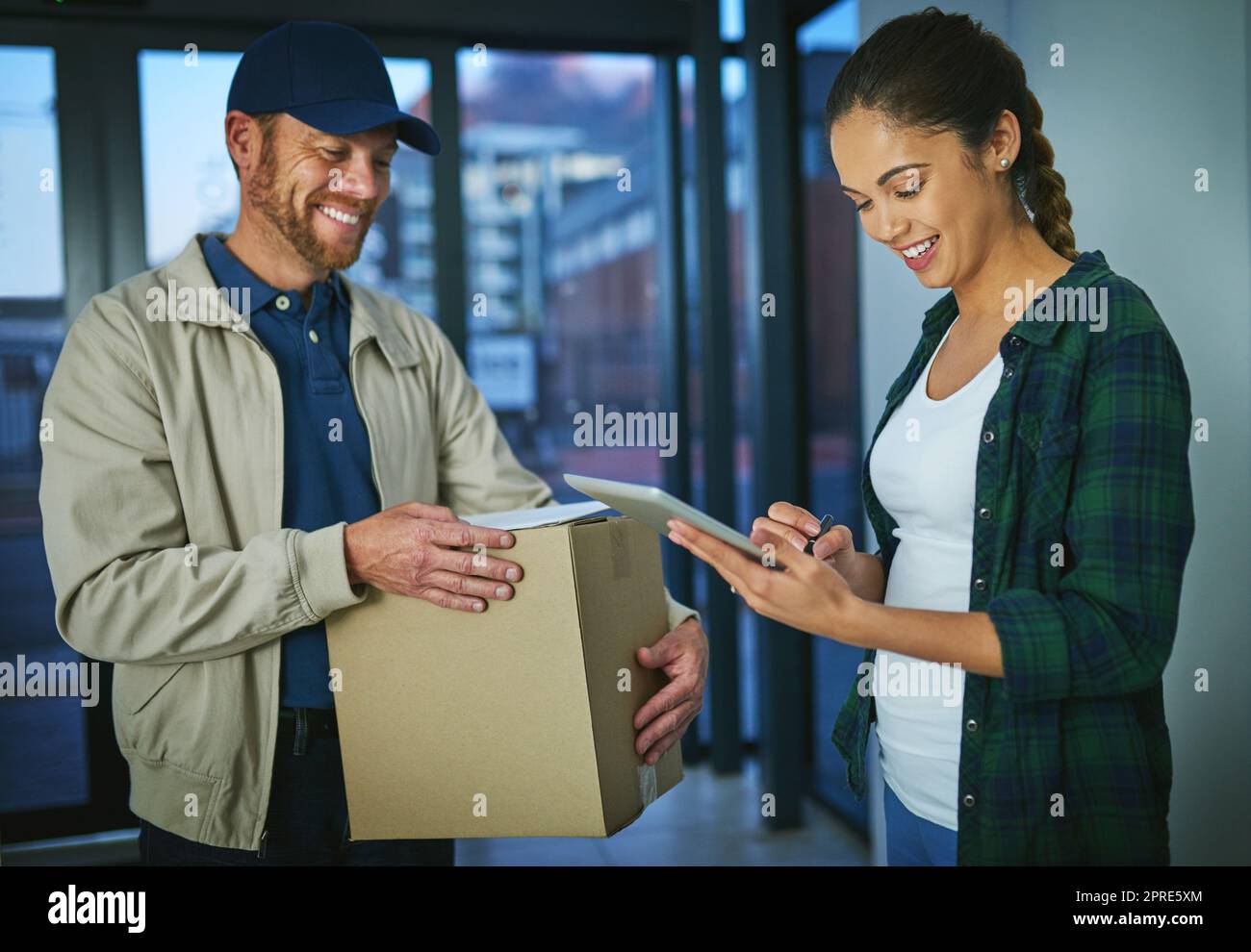No hay necesidad de papel cuando una firma electrónica va a ser útil. Una mujer joven usando una tableta digital para firmar un paquete de un hombre de parto. Foto de stock