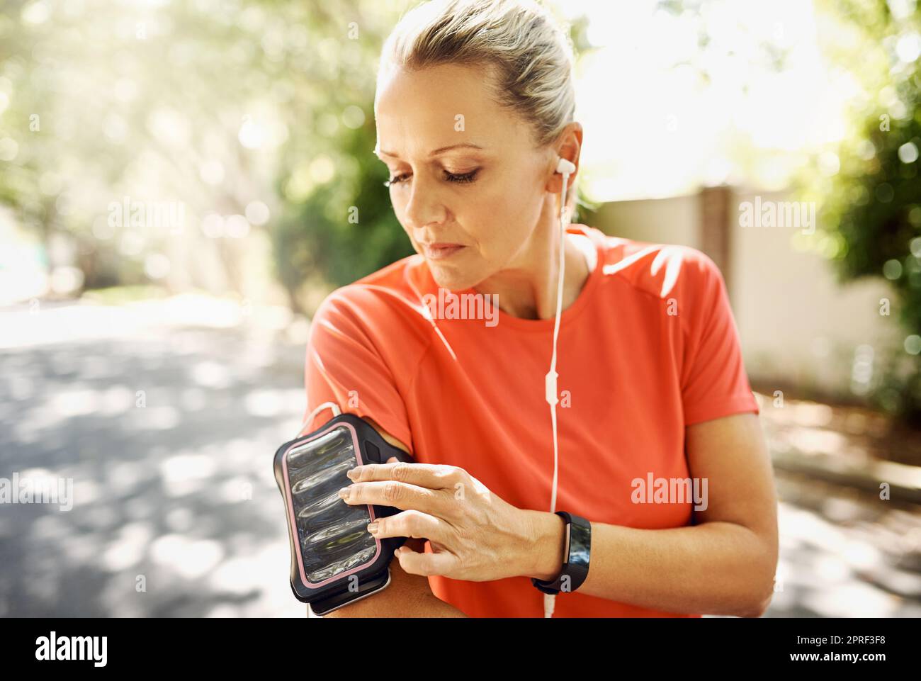 Mujer madura, activa y en forma escuchando música mientras corre afuera. Persona mayor motivada por su estilo de vida positivo y atlético. Entrenamiento femenino para evento deportivo o cuerpo de vacaciones de verano. Foto de stock