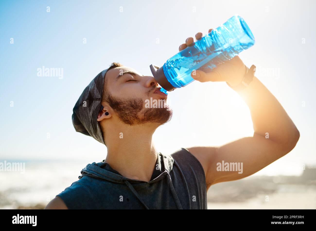 Su cuerpo no puede funcionar en su mejor si usted no hidrató. Un hombre joven deportivo que bebe agua mientras que ejercita al aire libre. Foto de stock