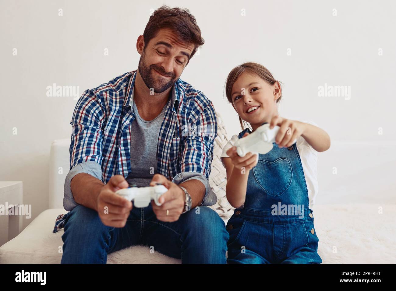 No, le di el único controlador que funciona: Un padre y su hija jugando videojuegos en casa. Foto de stock