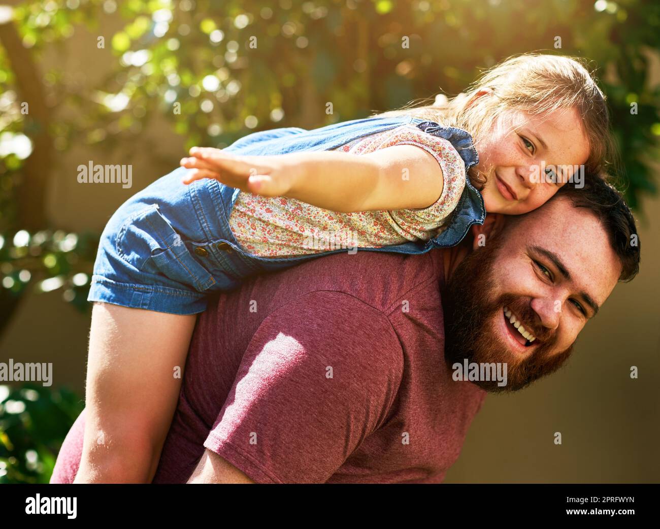 Con los papás apoyo concha volar lejos. Una adorable niña disfrutando de un paseo en piggyback de su padre en su patio trasero. Foto de stock