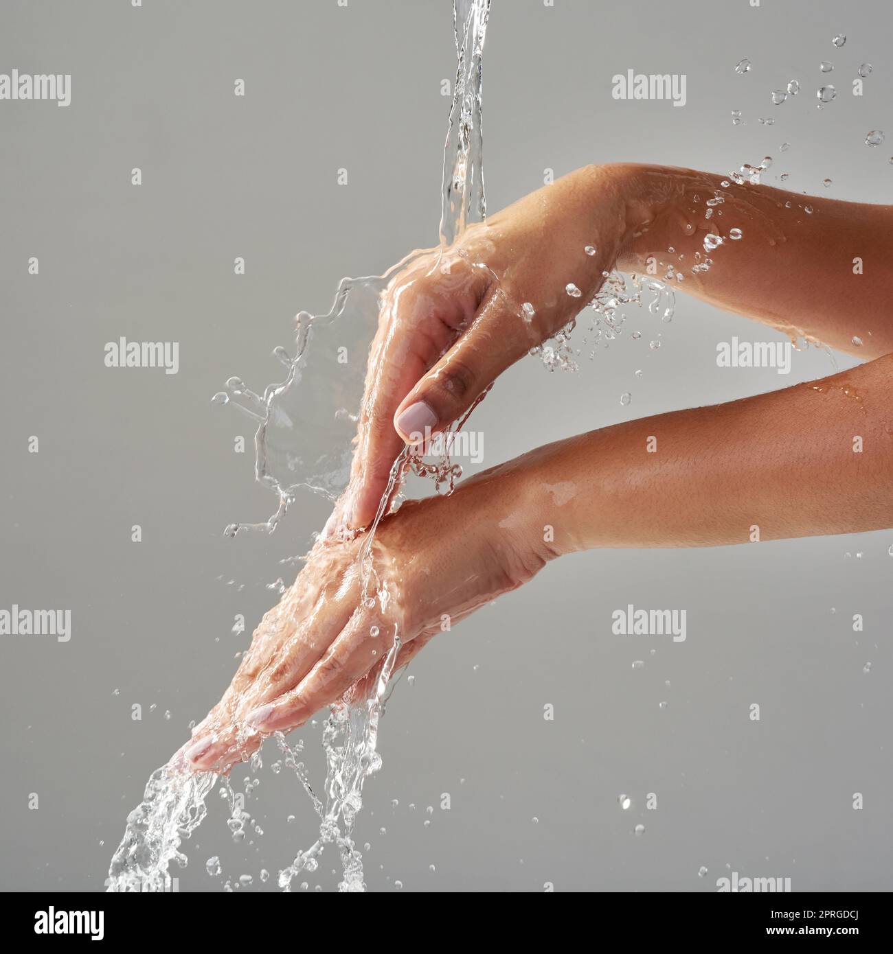 Lavándose y salpicando. Las manos se mantuvieron bajo un chorro de agua sobre un fondo gris. Foto de stock