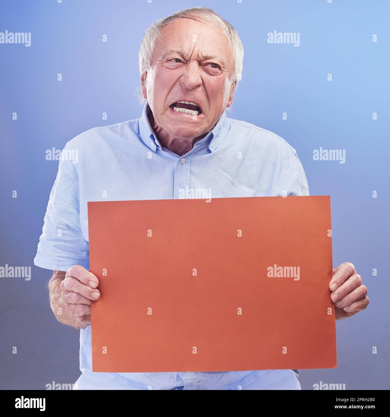 Grumpy te demostraré Grumpy. Tiro de estudio de un hombre mayor sosteniendo una señal en blanco y mirando infeliz contra un fondo azul Foto de stock