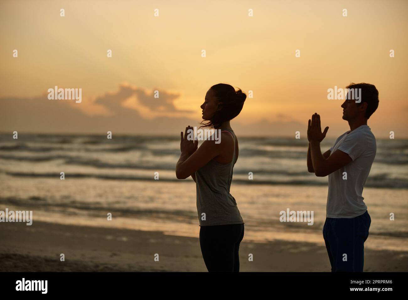 Lograr la salud y la felicidad a través del yoga. Una pareja haciendo yoga en la playa al atardecer. Foto de stock