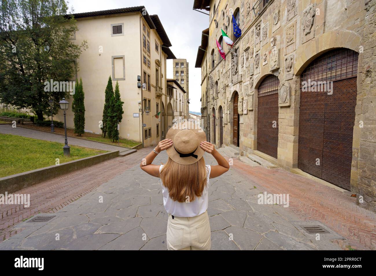 Vacaciones en Italia. Vista trasera de la hermosa chica viajero que sostiene sombrero disfruta visitando la histórica ciudad de Arezzo, Toscana, Italia. Foto de stock