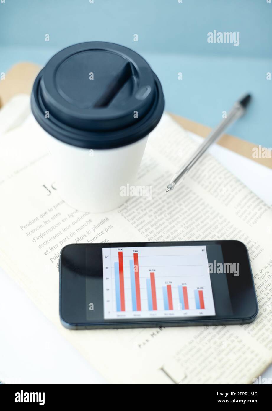Oficina portátil. Smartphone con barra en la pantalla sentado en la parte superior de un periódico y portapapeles con una taza y un bolígrafo desechables. Foto de stock