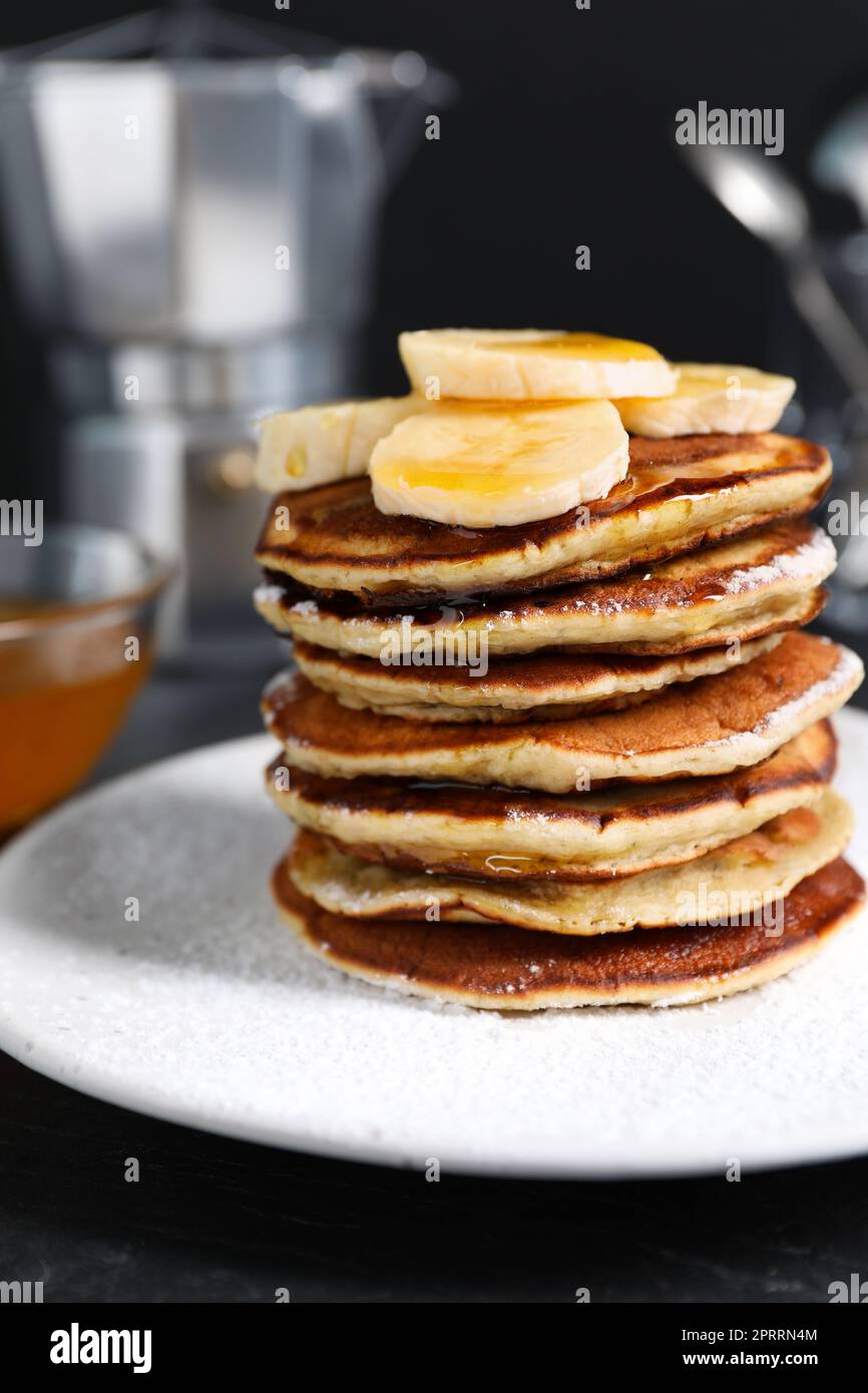 Plato de panqueques de plátano con miel y azúcar en polvo sobre mesa negra, primer plano Foto de stock