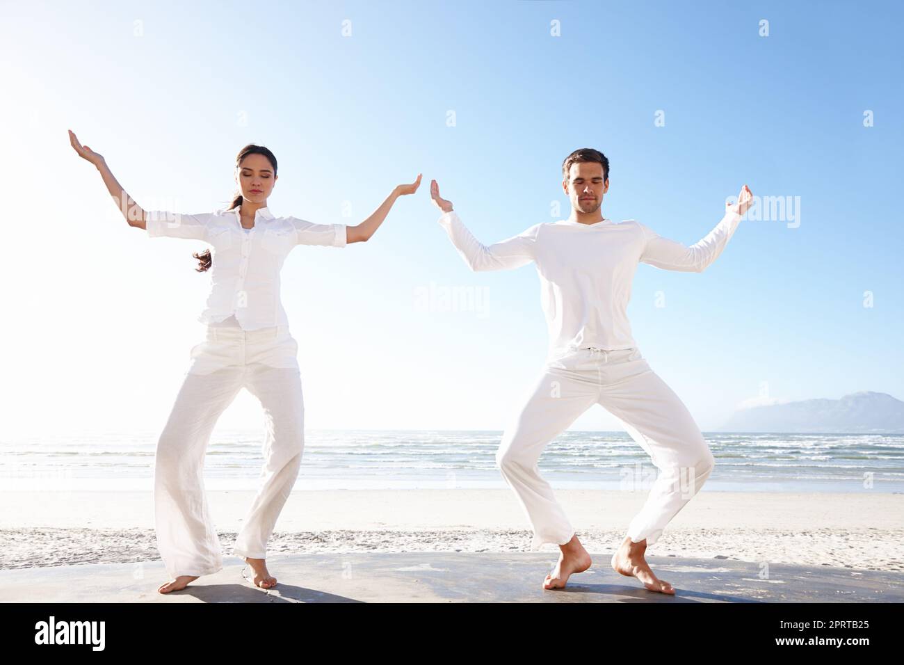 Yoga junto a la belleza de la naturaleza. Plano completo de un hombre y una mujer joven haciendo yoga junto al mar. Foto de stock