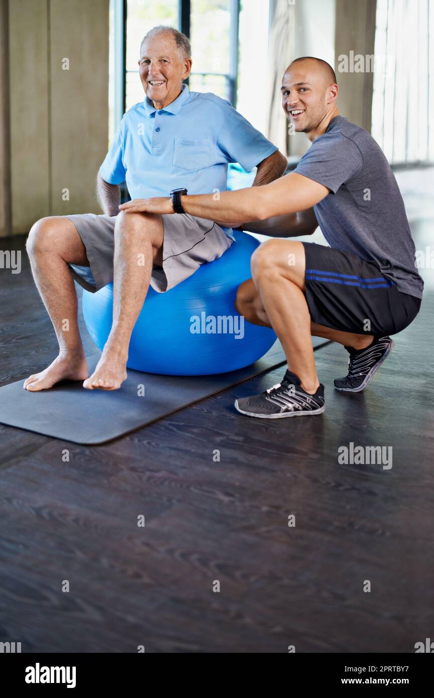 Él consigue más fuerte cada día. Un amaestrador personal guapo con un hombre mayor. Foto de stock