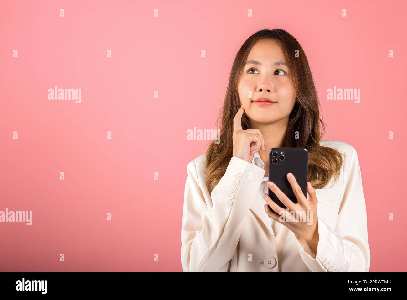 mujer joven emocionada sonriente sosteniendo el teléfono móvil y piensa la cara del tacto del dedo de la idea Foto de stock