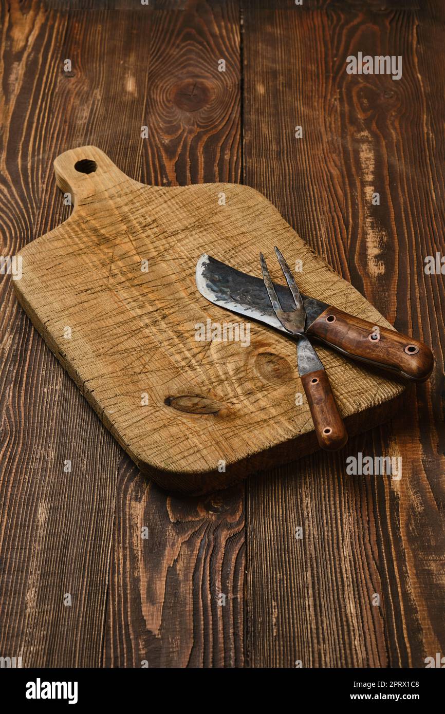 Tabla de cortar vieja rústica con cuchillo forjado y tenedor Foto de stock