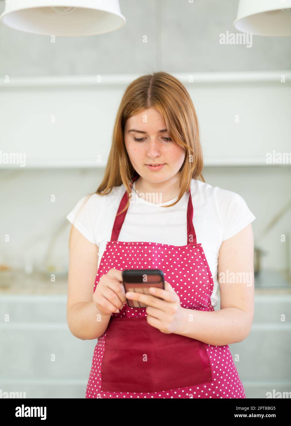 Retrato de chica adolescente enfocada con delantal de lunares rojos y  buscando receta en el teléfono inteligente en la cocina moderna en el  interior Fotografía de stock - Alamy