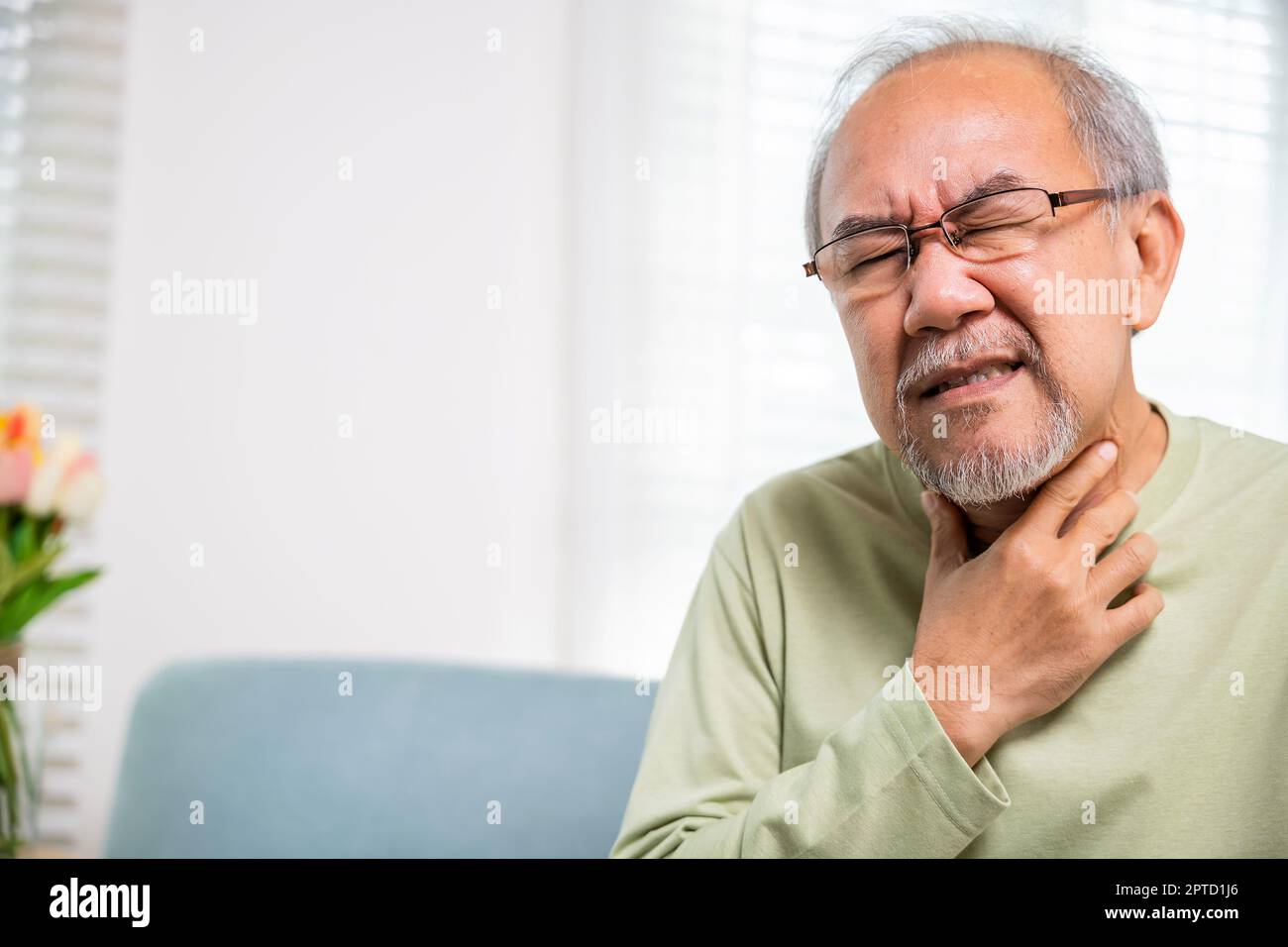 Viejo asiático doloroso en la garganta dolorida, anciano del retiro sintiendo dolor usar las manos sosteniendo el cuello, las personas mayores tienen disfagia debido a comer, curan Foto de stock