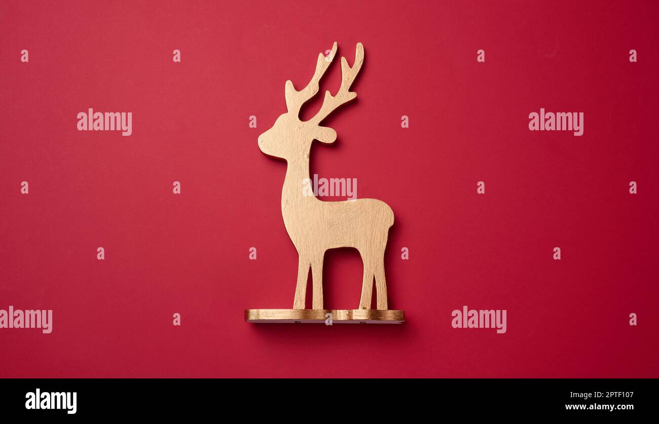 Juguete de ciervo de madera dorada sobre fondo rojo, vista desde arriba. Decoración de Navidad Foto de stock