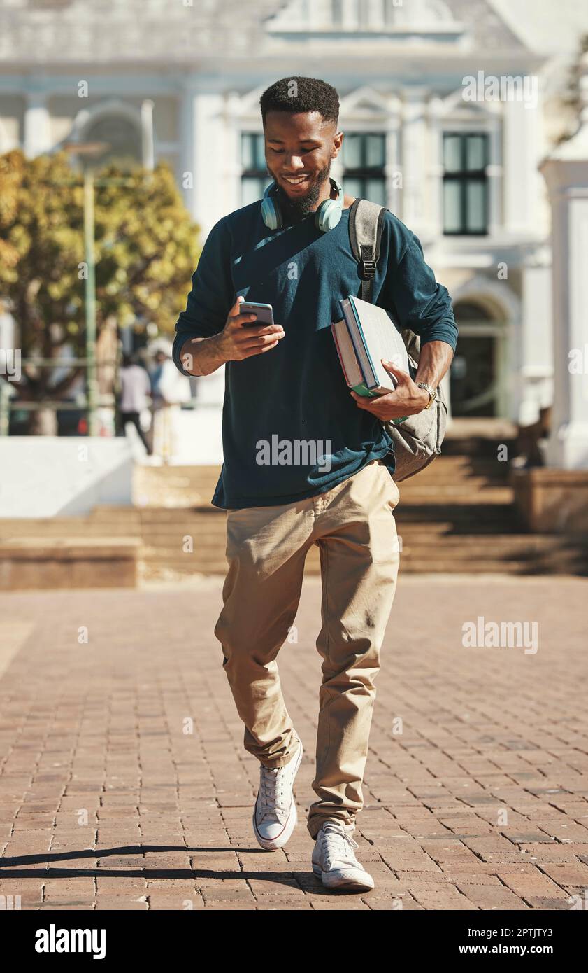 Universidad, educación y teléfono con un hombre negro estudiante escribir un mensaje de texto mientras lleva libros. Contacto, estudio y beca con un alumno masculino Foto de stock