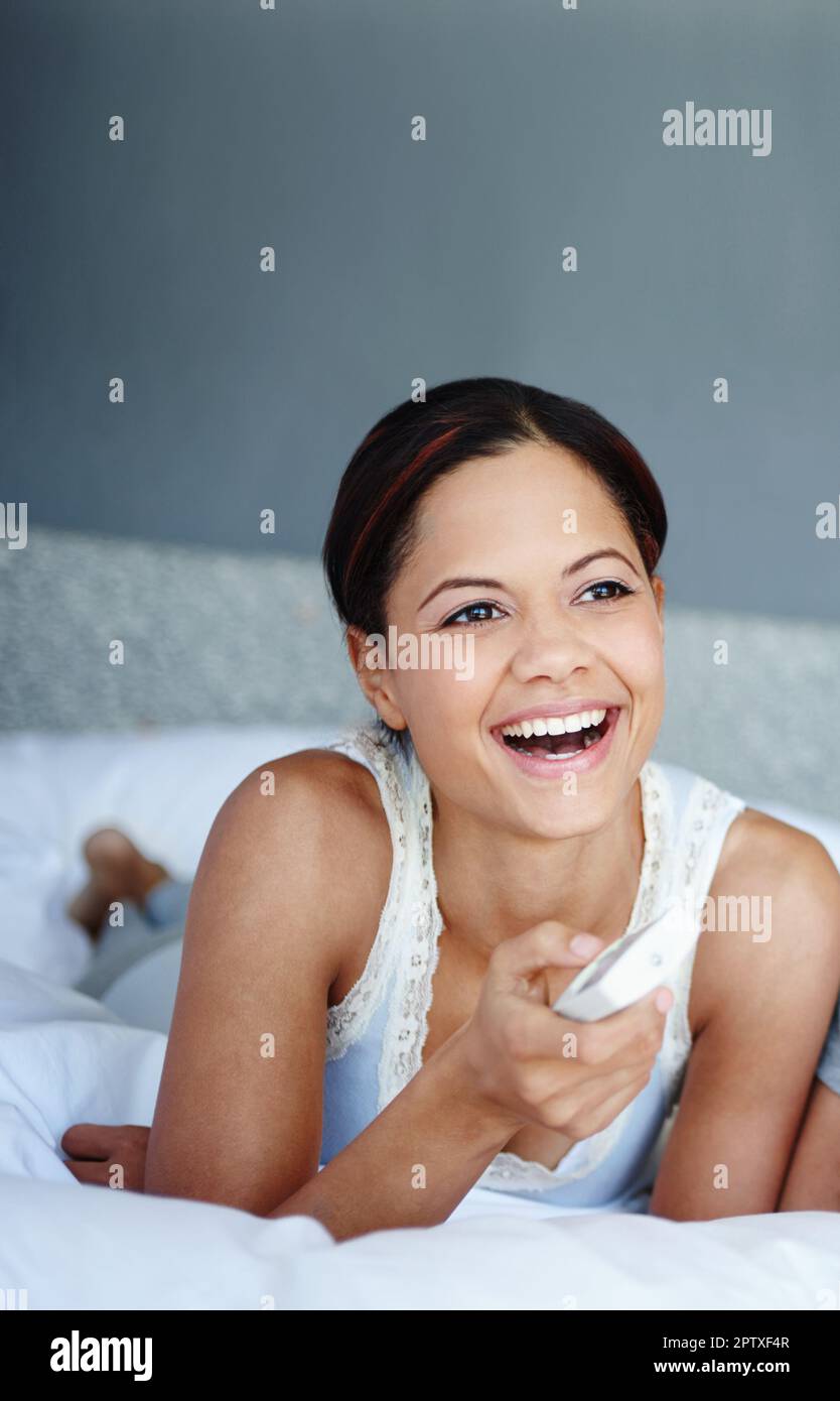 Me encanta esta película. una mujer riendo mujer con un control remoto en  la mano acostada en su cama Fotografía de stock - Alamy