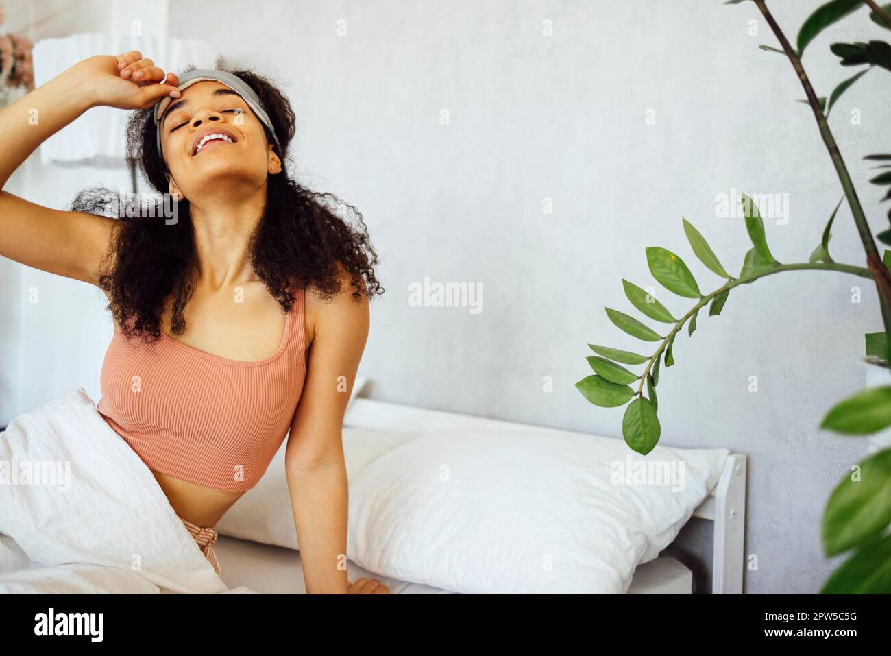 Mujer joven afroamericana usa pijama durmiendo en la cama en casa, con los ojos cerrados, tomando un descanso. Chica millennial negra descansando, despierta en el Foto de stock
