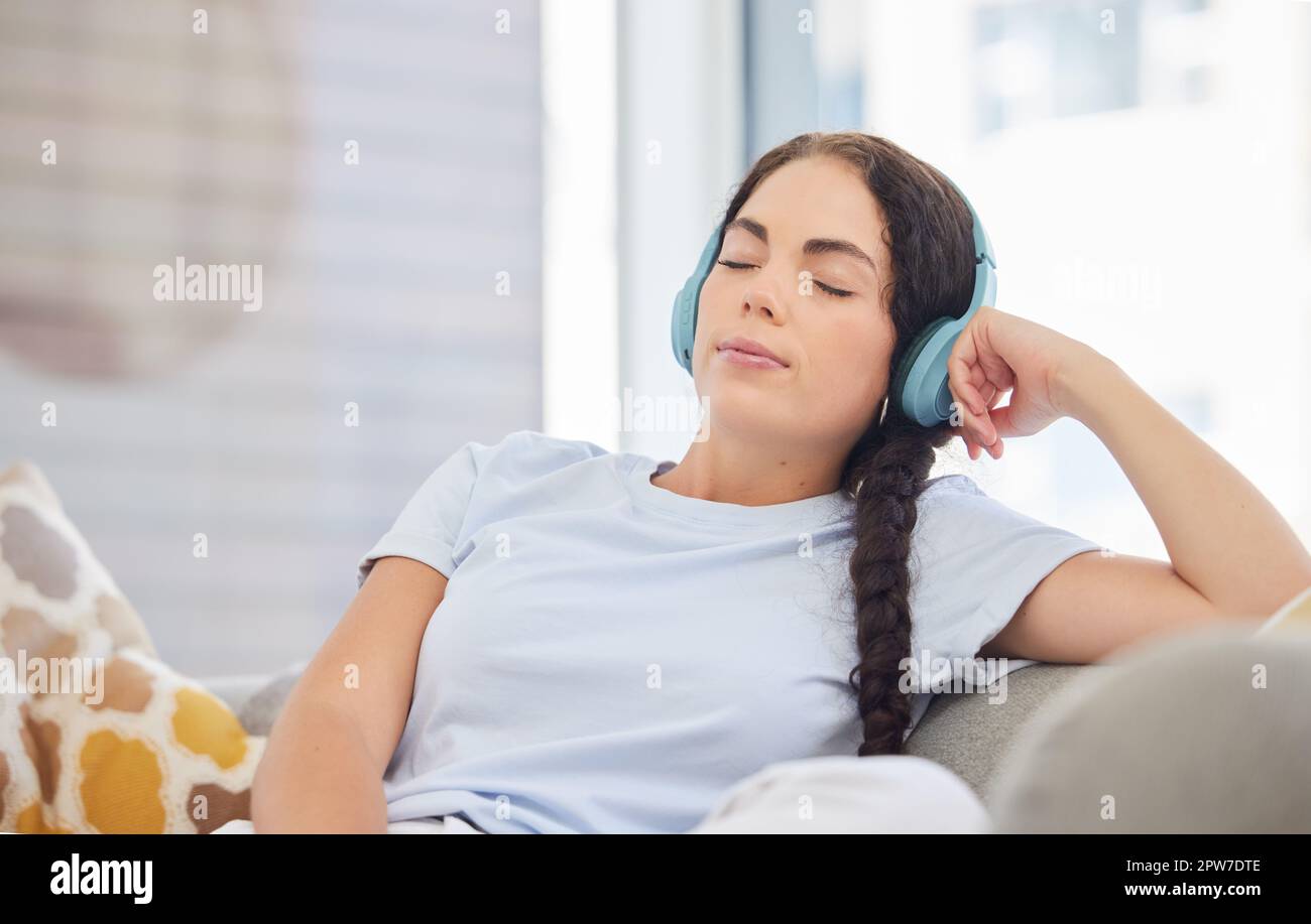 Auriculares, relax y mujer joven en un sofá escuchando música tranquila,  radio o podcast en su sala de estar. Paz, zen y cómoda dama streaming au  Fotografía de stock - Alamy