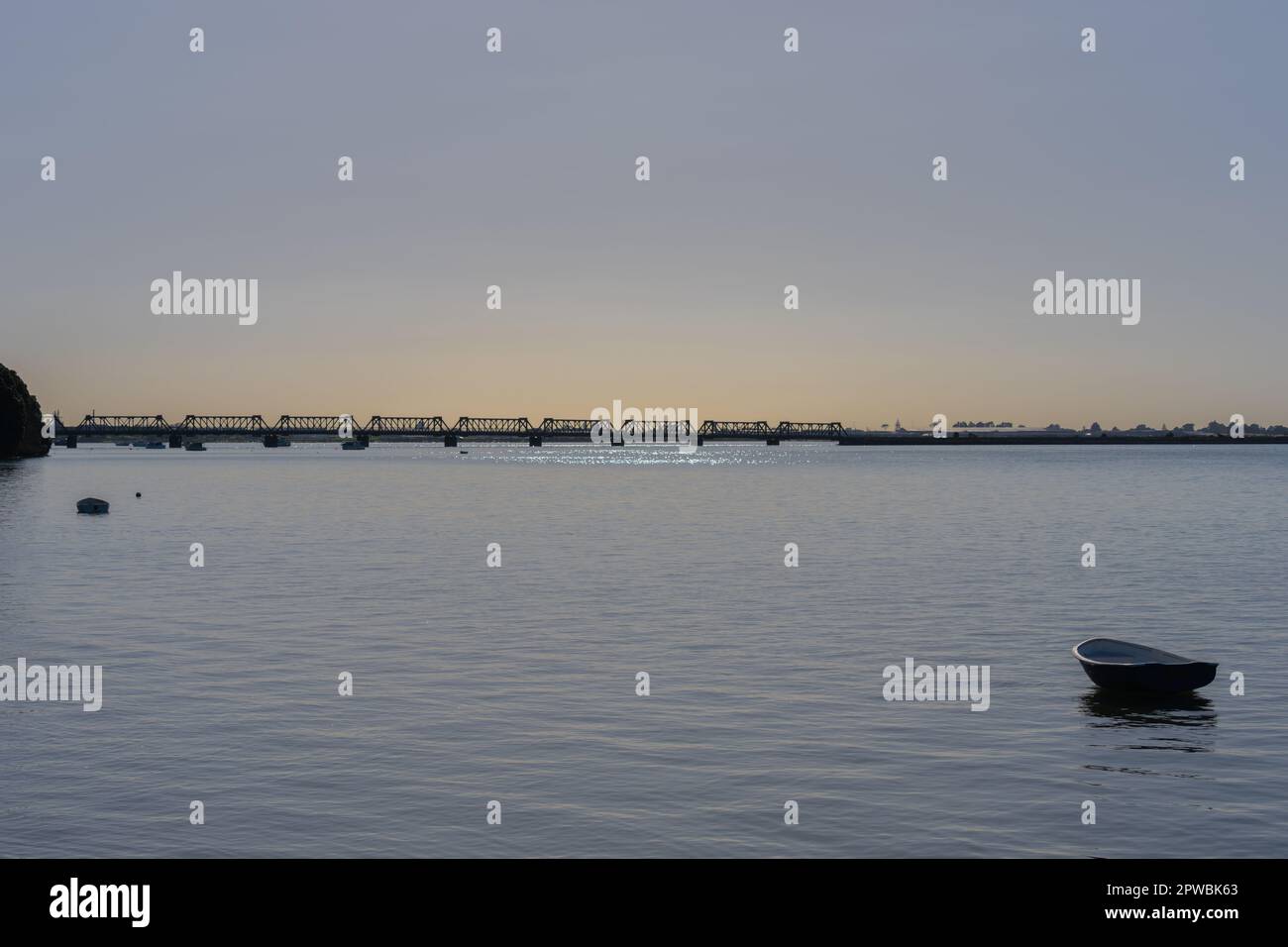 Crepúsculo sobre el puerto de Tauranga con el truss distante del puente ferroviario cielo azul pálido y ligero tono dorado en el horizonte Foto de stock
