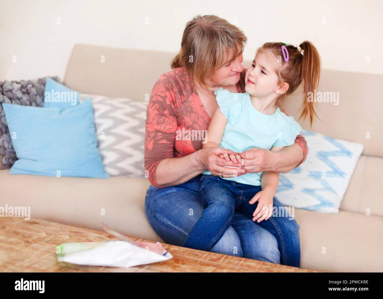 Corta las manos desinfectadas de la nieta con un paño húmedo antibacteriano mientras se sienta en el sofá en casa Foto de stock