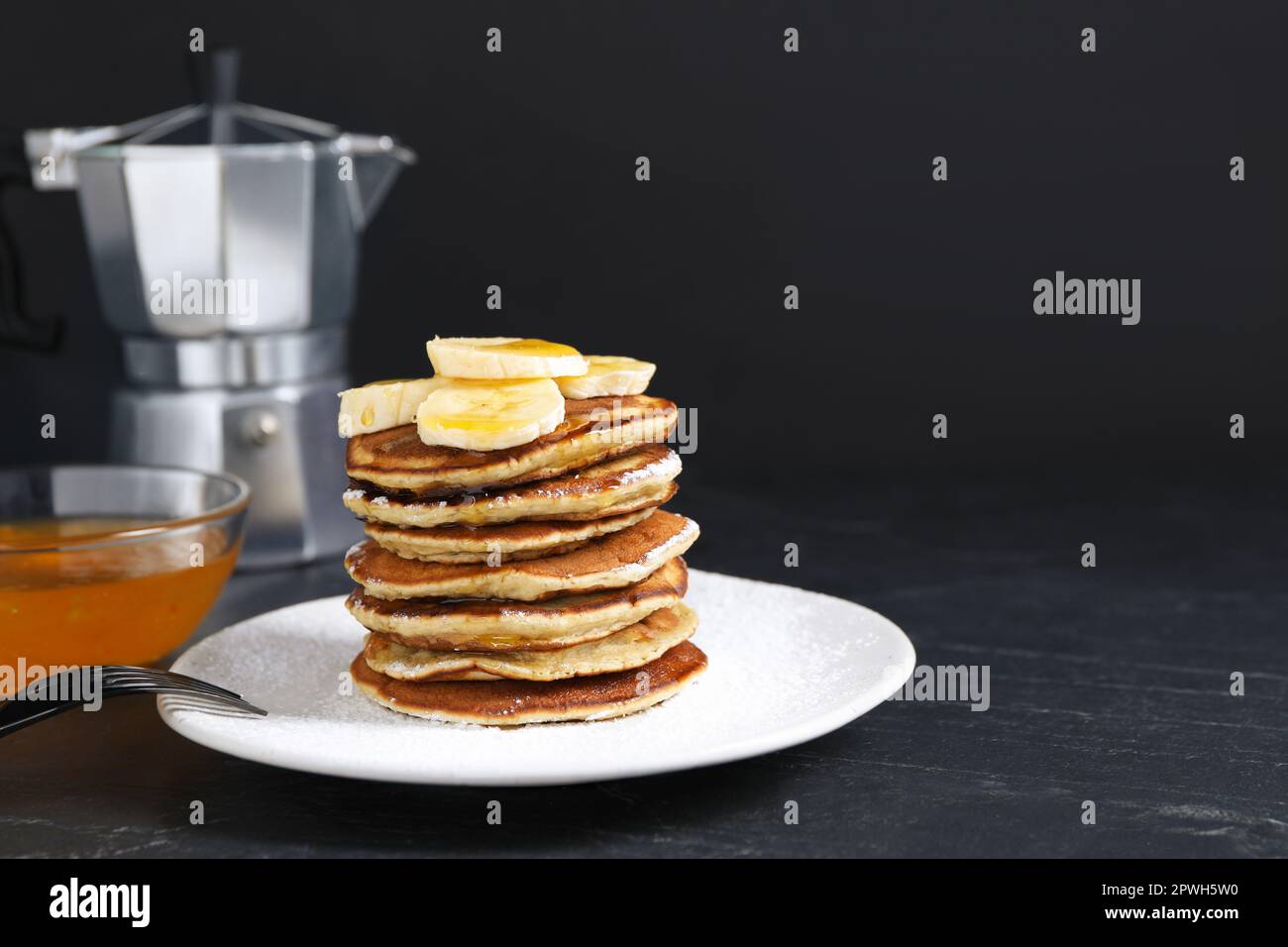 Plato de panqueques de plátano con miel y azúcar en polvo servido en mesa negra. Espacio para texto Foto de stock