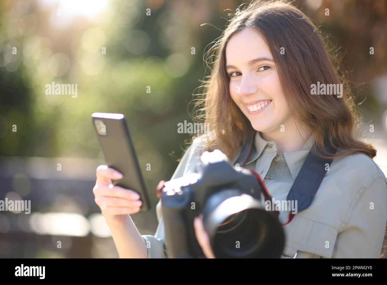 Fotógrafo feliz emparejando el teléfono celular con la cámara profesional dslr que te mira Foto de stock