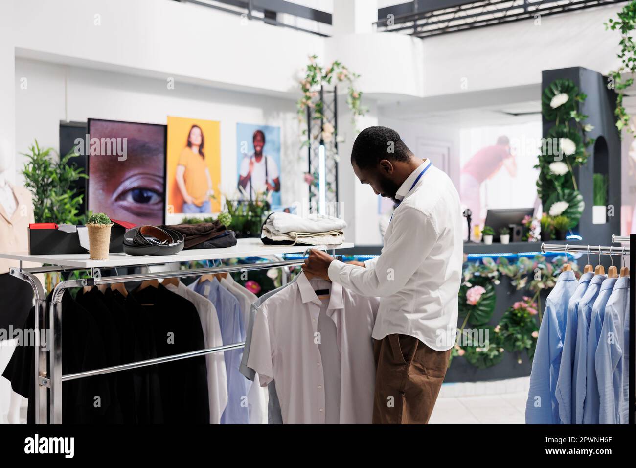 Ropa de centro comercial hombre asistente colgando camisas en el estante,  mostrando ropa para la venta. Boutique de moda empleado afroamericano que  muestra la ropa masculina para los clientes Fotografía de stock -