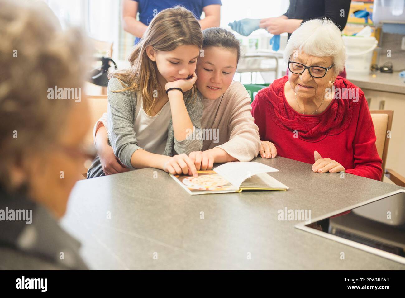 Mujeres mayores con niñas leyendo libro en casa de descanso Foto de stock