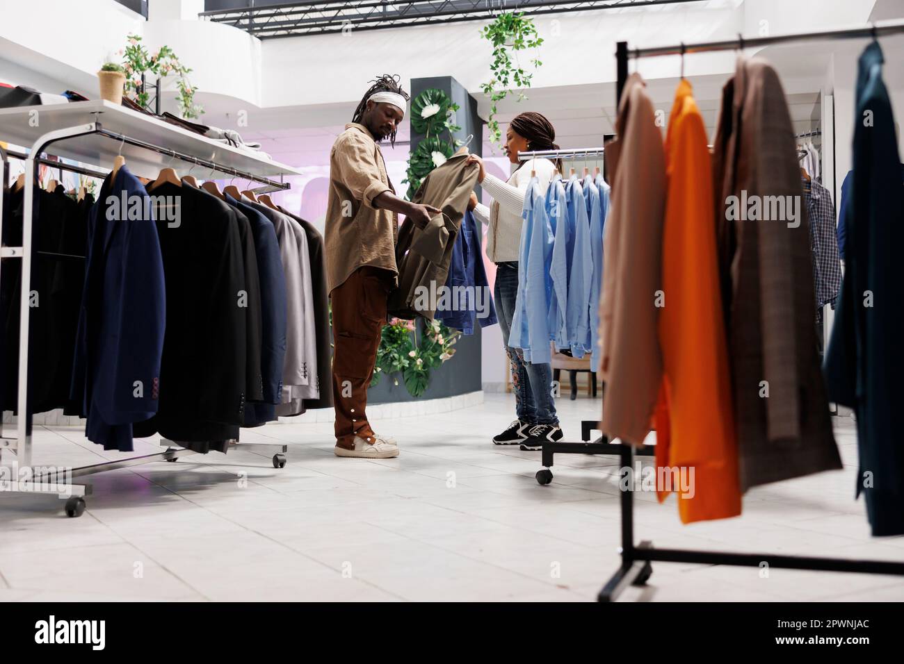 Zoológico de noche Hermano Sombra Hombre y mujer afroamericanos comprando ropa en el centro comercial y  decidiendo entre dos chaquetas en perchas. Clientes de novio y novia que  eligen ropa formal en la tienda Fotografía de stock -