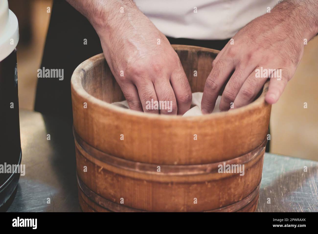 Primer plano de las manos de un irreconocible chef de sushi cocinando arroz en un recipiente o cubo de vapor asiático de madera tradicional Foto de stock