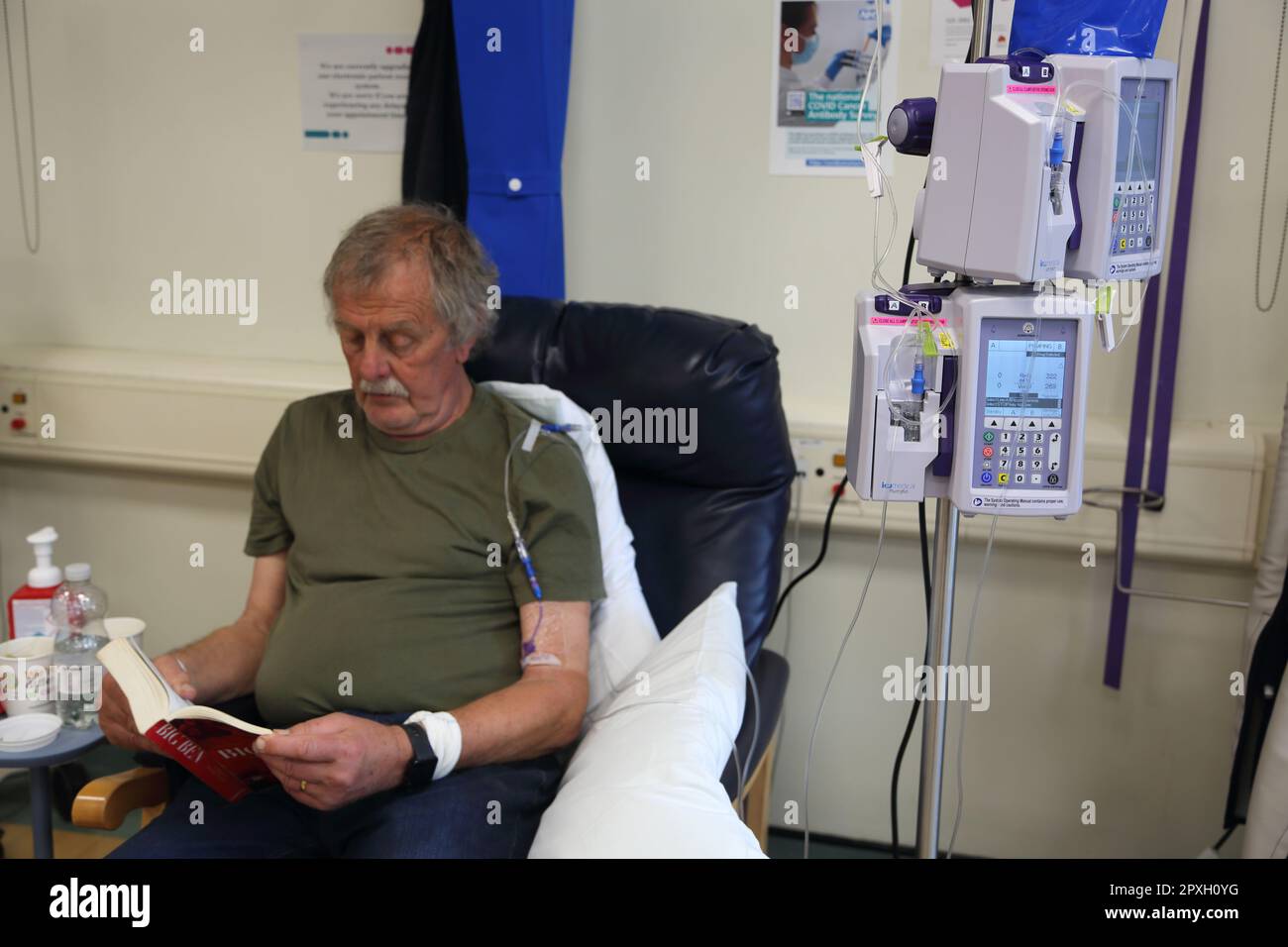 Libro de lectura de pacientes de cáncer mientras se está recibiendo tratamiento de quimioterapia con infusión intravenosa Bomba de quimioterapia Surrey England Foto de stock