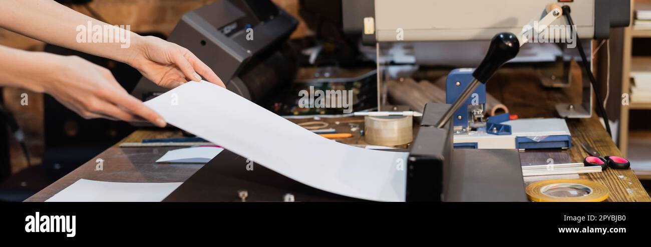 vista recortada de la mujer sosteniendo el papel junto al recortador de papel en el centro de impresión, bandera, imagen de stock Foto de stock