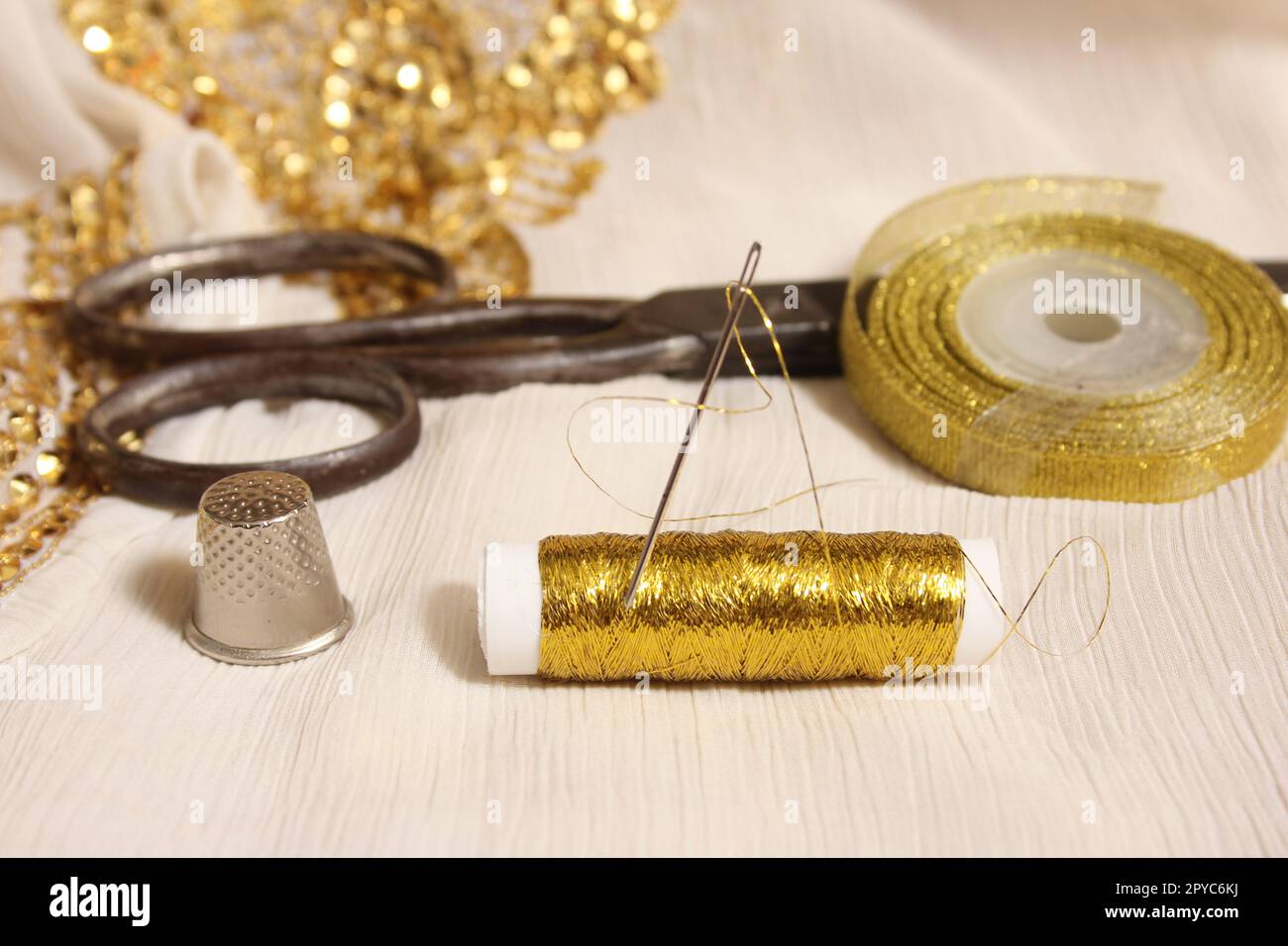 Carrete de hilo metálico de oro y tijeras con dedal en tela blanca con  lentejuelas de oro Fotografía de stock - Alamy