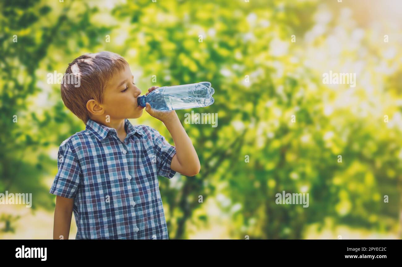 Lindo niño bebiendo una botella de agua pura en la naturaleza. Foto de stock