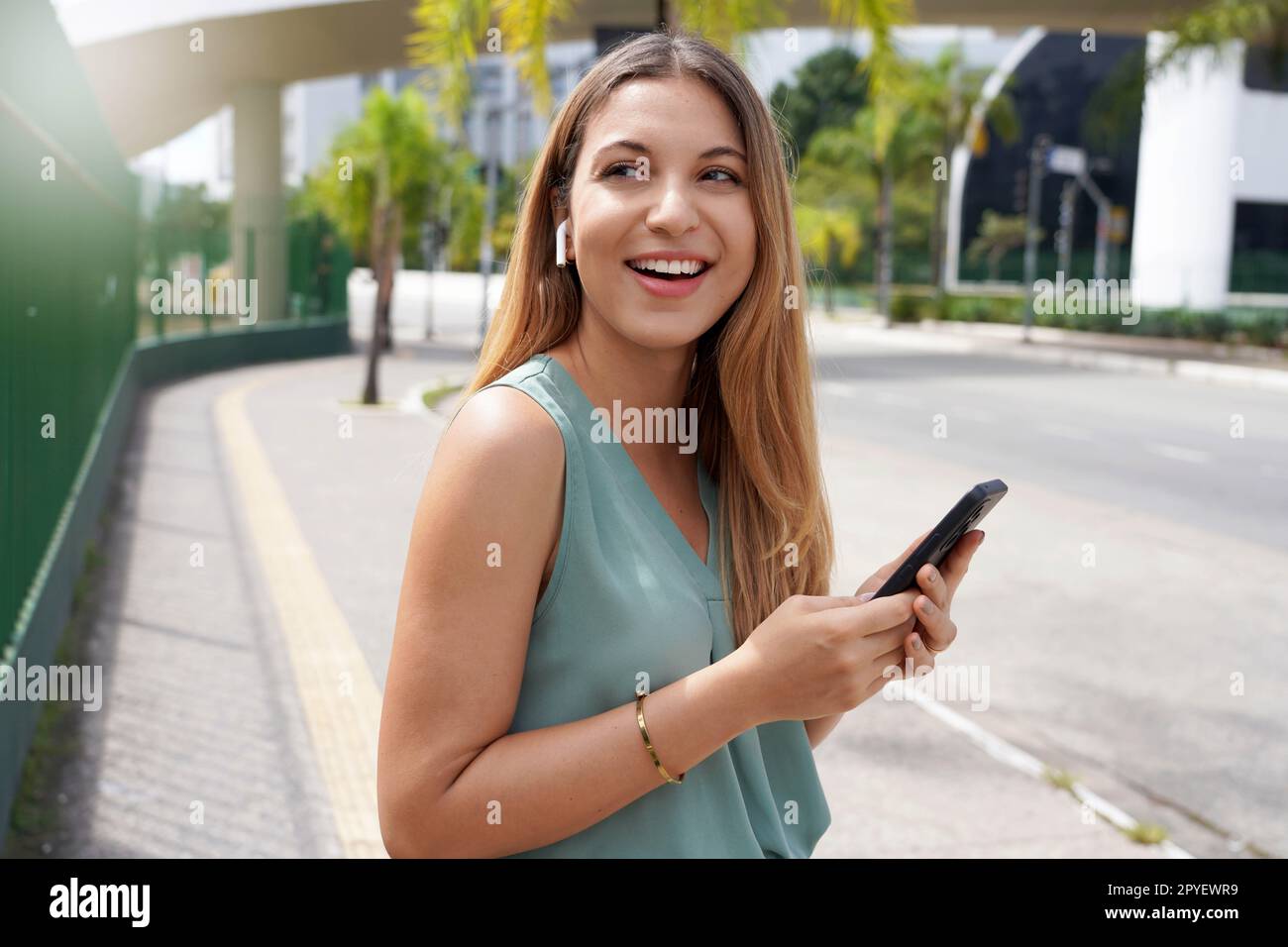 Hermosa chica brasileña usando auriculares inalámbricos para escuchar música en la calle de la ciudad Foto de stock