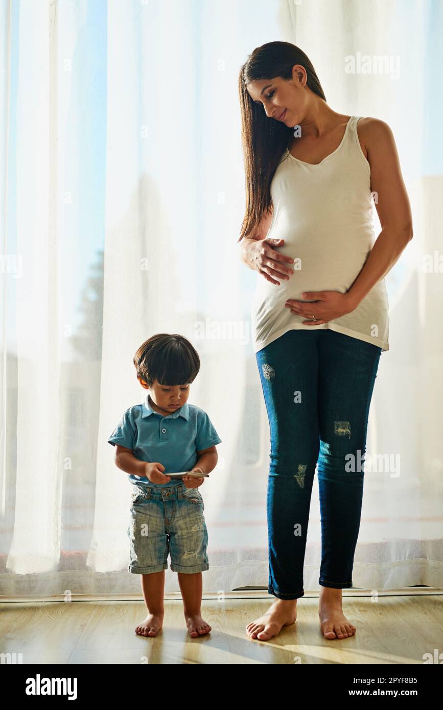 La tecnología inalámbrica hace que sea una niñera fantástica. una mujer embarazada mirando a su niño pequeño mientras juega con un teléfono inteligente. Foto de stock