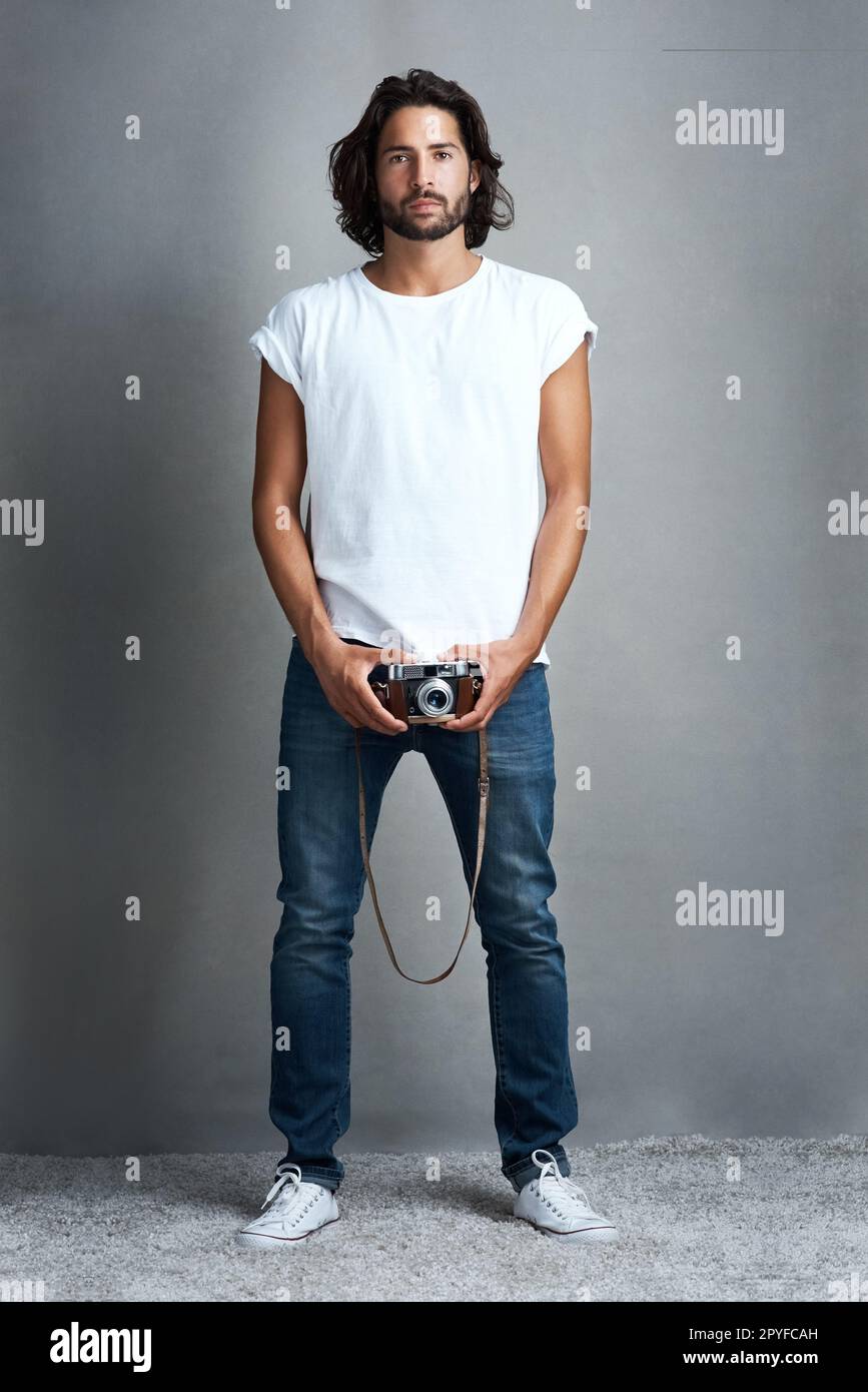 Ten en cuenta si tomo tu foto. Retrato de estudio de un hombre joven posando con una cámara vintage contra un fondo gris. Foto de stock