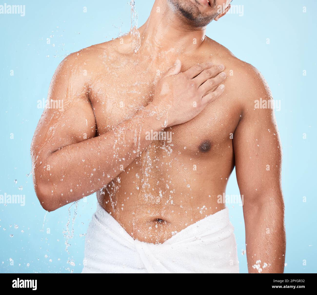 Cuerpo, agua y ducha con un modelo de hombre de pie en el estudio sobre un fondo azul para la higiene o la hidratación. Splash, salud y bienestar con un hombre que lleva una toalla en el baño después del baño Foto de stock