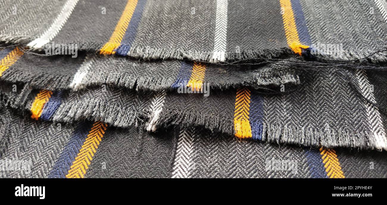 Tejido gris-negro con rayas naranjas y azules. Tela textil doblada cuidadosamente en la superficie. Material de lana natural para coser ropa y tapicería. Estilo de vida. Primer plano. Enfoque suave Foto de stock