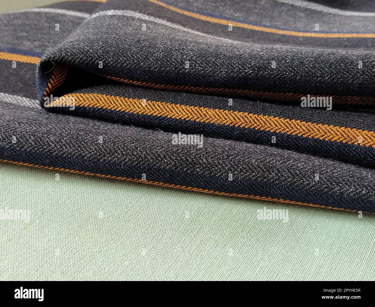 Tejido gris-negro con rayas naranjas y azules. Tela textil doblada cuidadosamente en la superficie. Material de lana natural para coser ropa y tapicería. Estilo de vida. Primer plano. Enfoque suave Foto de stock
