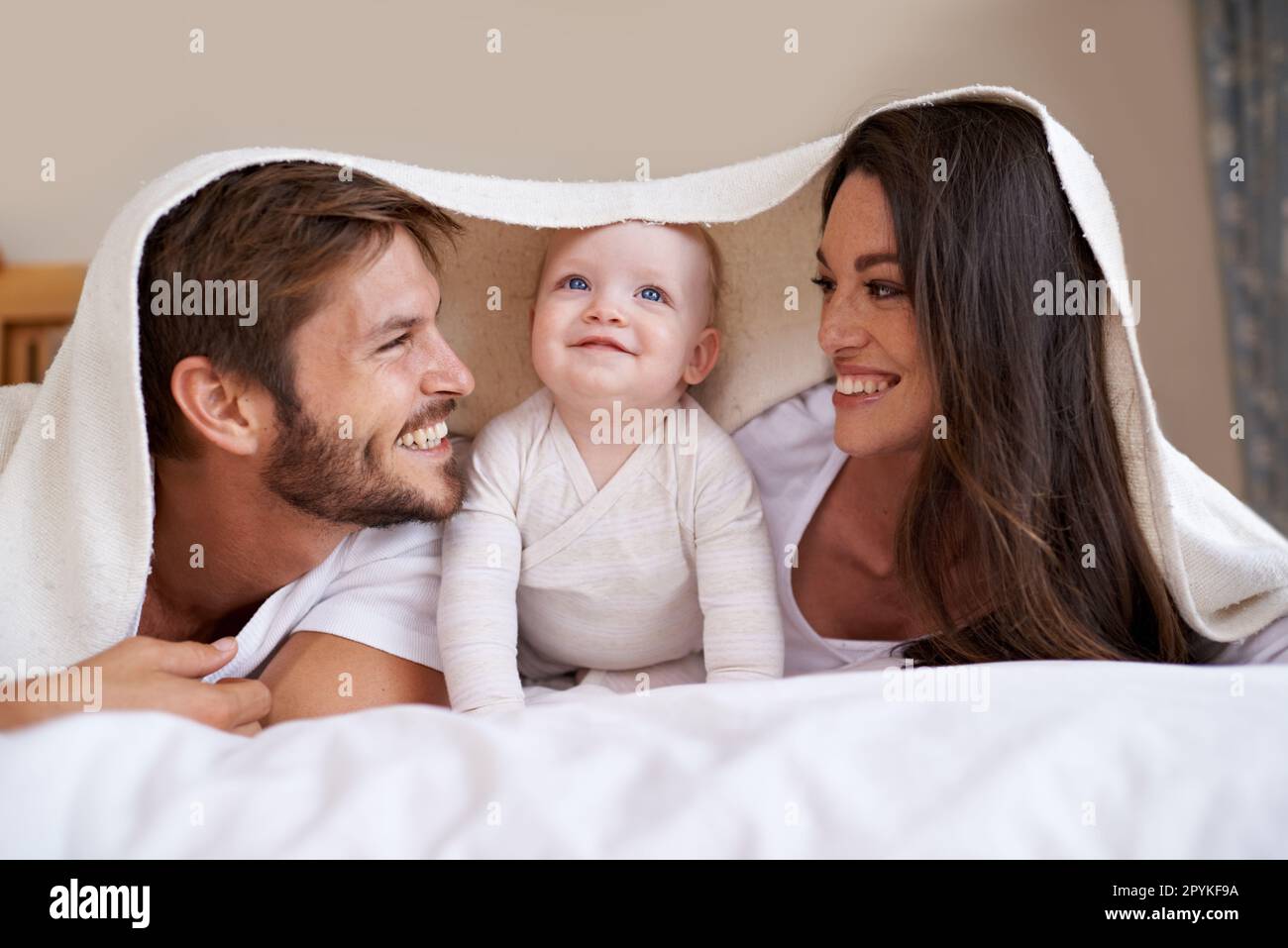 Familia feliz, padres y bebé con manta en la cama para el amor, el cuidado y el tiempo de