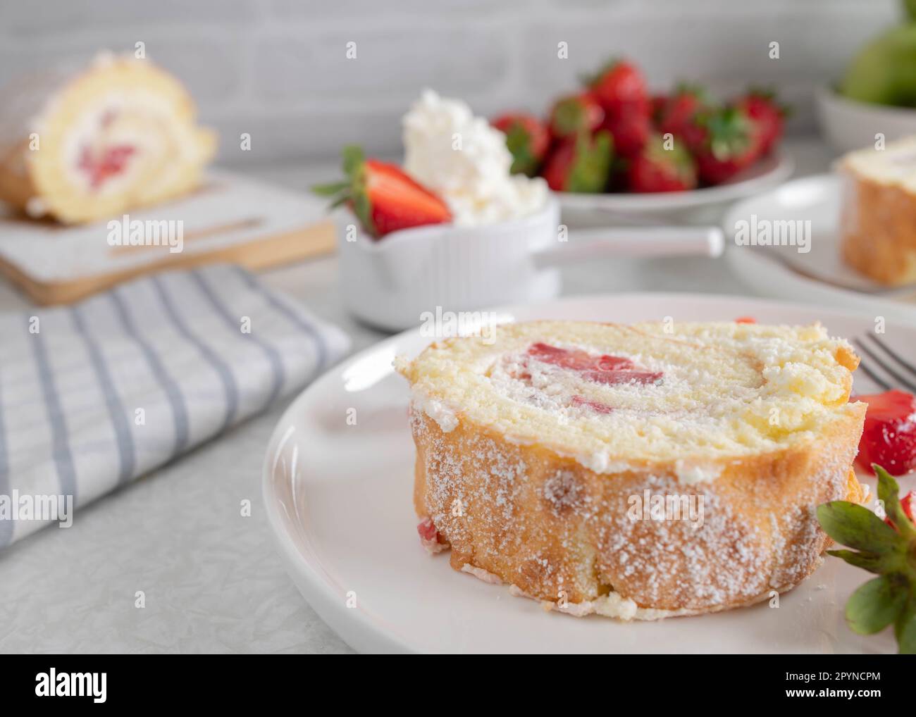 Rebanada de rollo suizo con crema batida y relleno de fresa en un plato sobre fondo claro Foto de stock