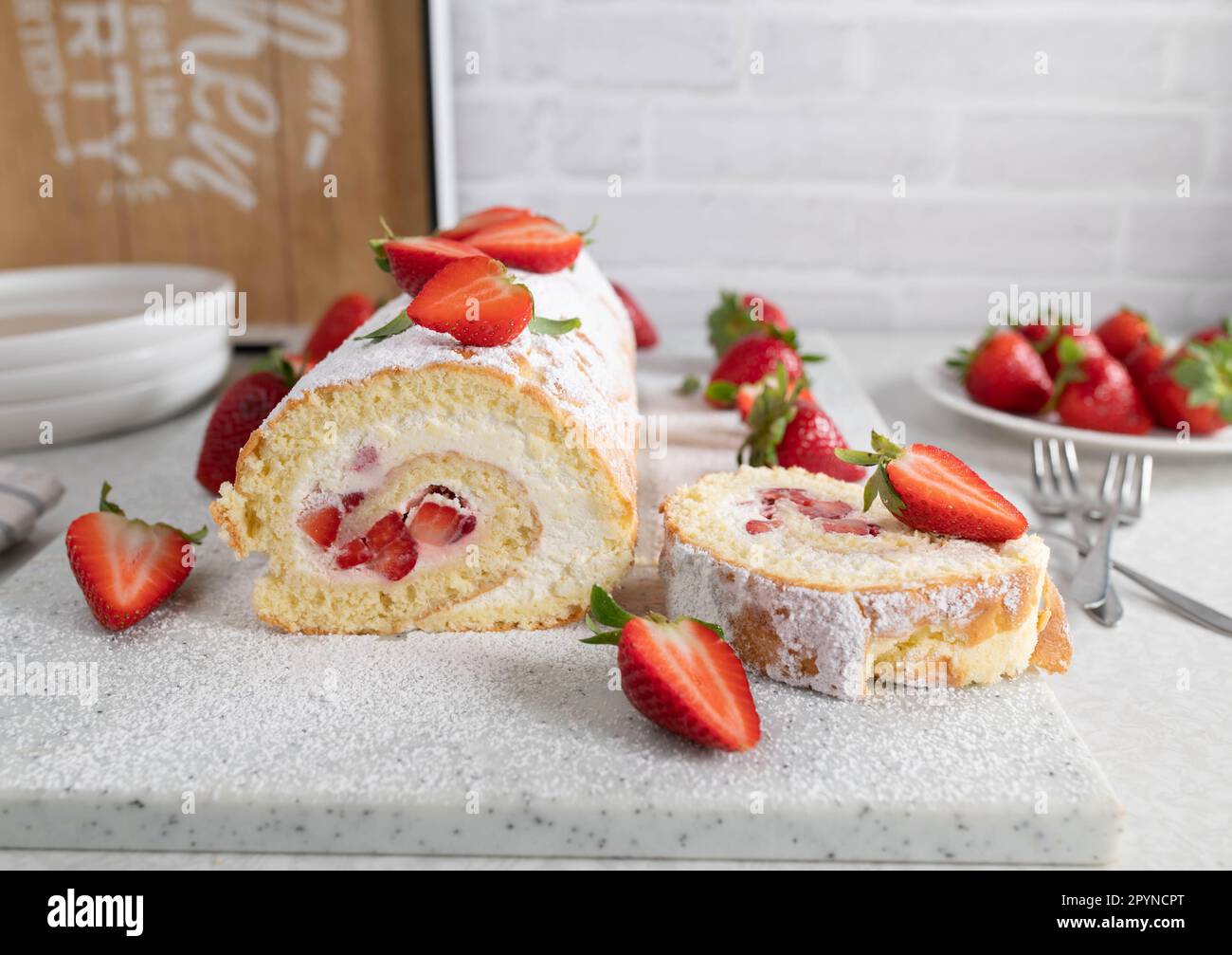 Rollo suizo con crema batida y relleno de fresa sobre fondo de cocina ligera Foto de stock