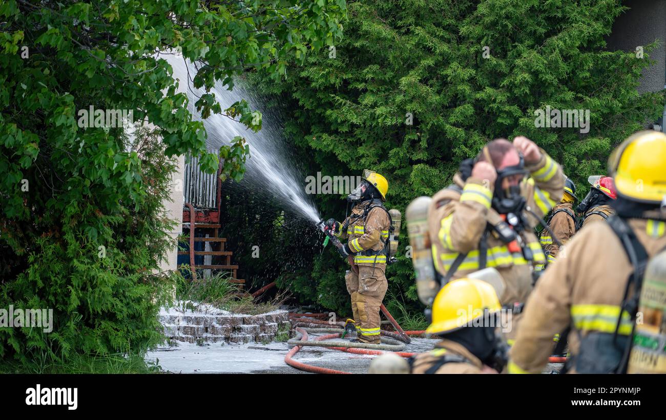 Bombero luchando contra un incendio doméstico con un grupo de bomberos que se preparan para luchar Foto de stock