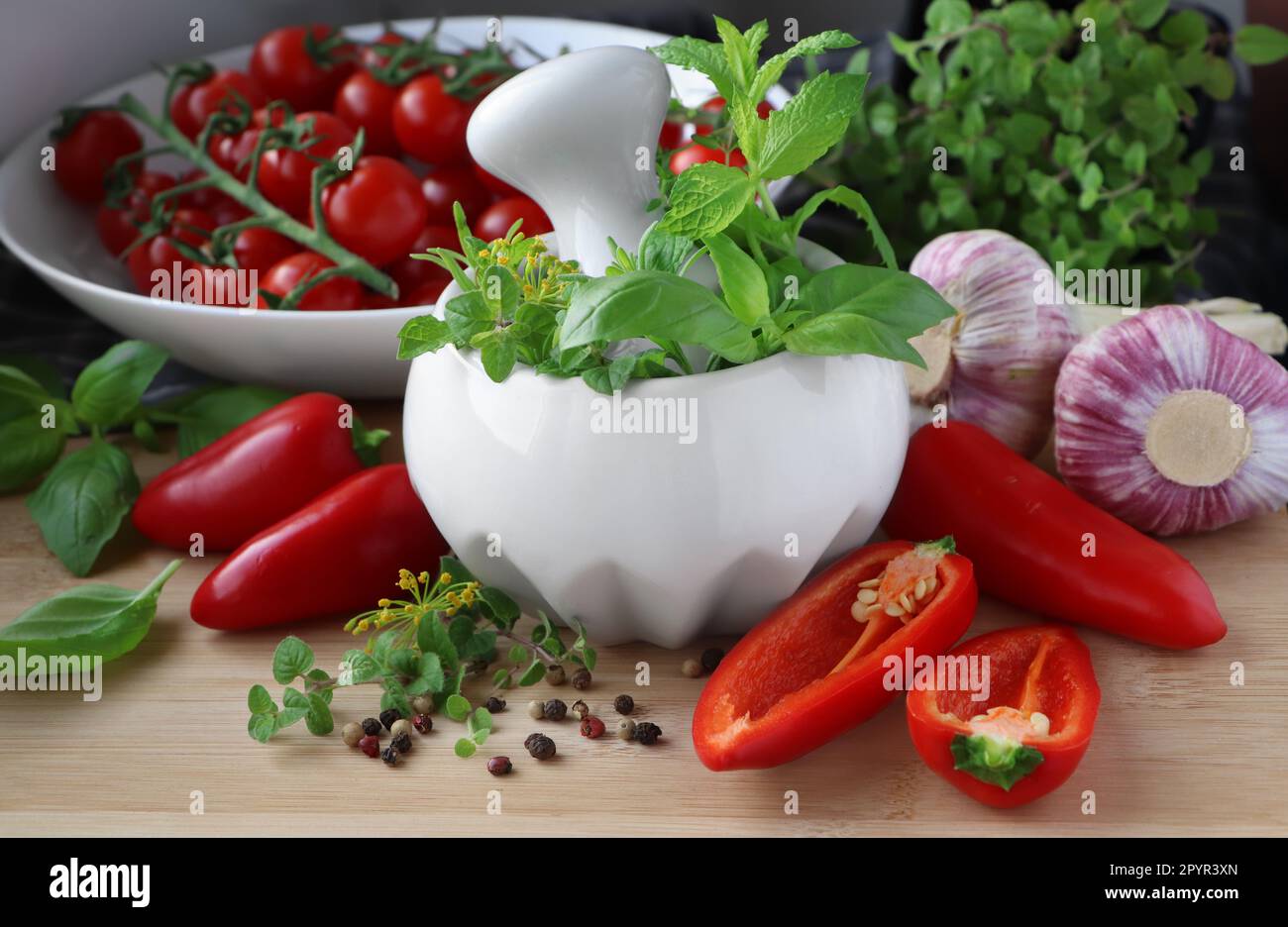 Mortero con hierbas frescas cerca de ajo, pimienta y tomates cherry en la mesa de madera, primer plano Foto de stock