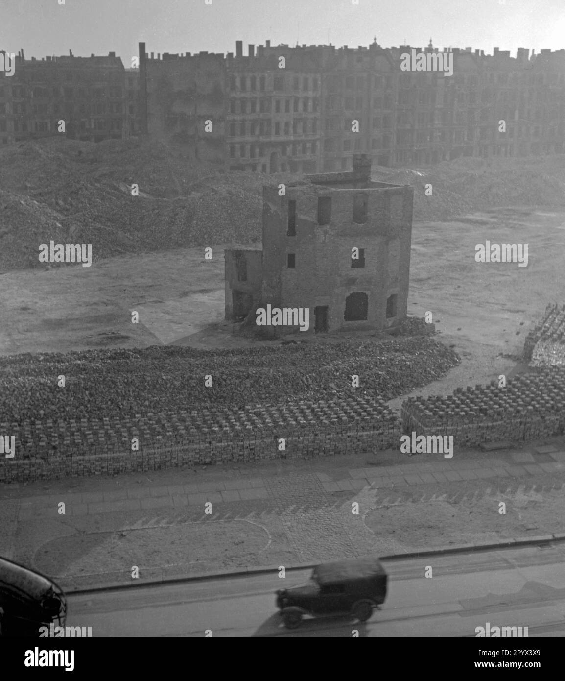 Foto sin fecha de una zona abandonada casi completamente devastada en Berlín, presumiblemente Berlín Occidental, 1950. En la superficie, los ladrillos derribados apilados para la construcción de nuevas casas. En el medio, una parte parcialmente destruida de un edificio residencial. En primer plano, una carretera con coches que pasan. En el fondo, destruyó bloques de pisos. Foto de stock